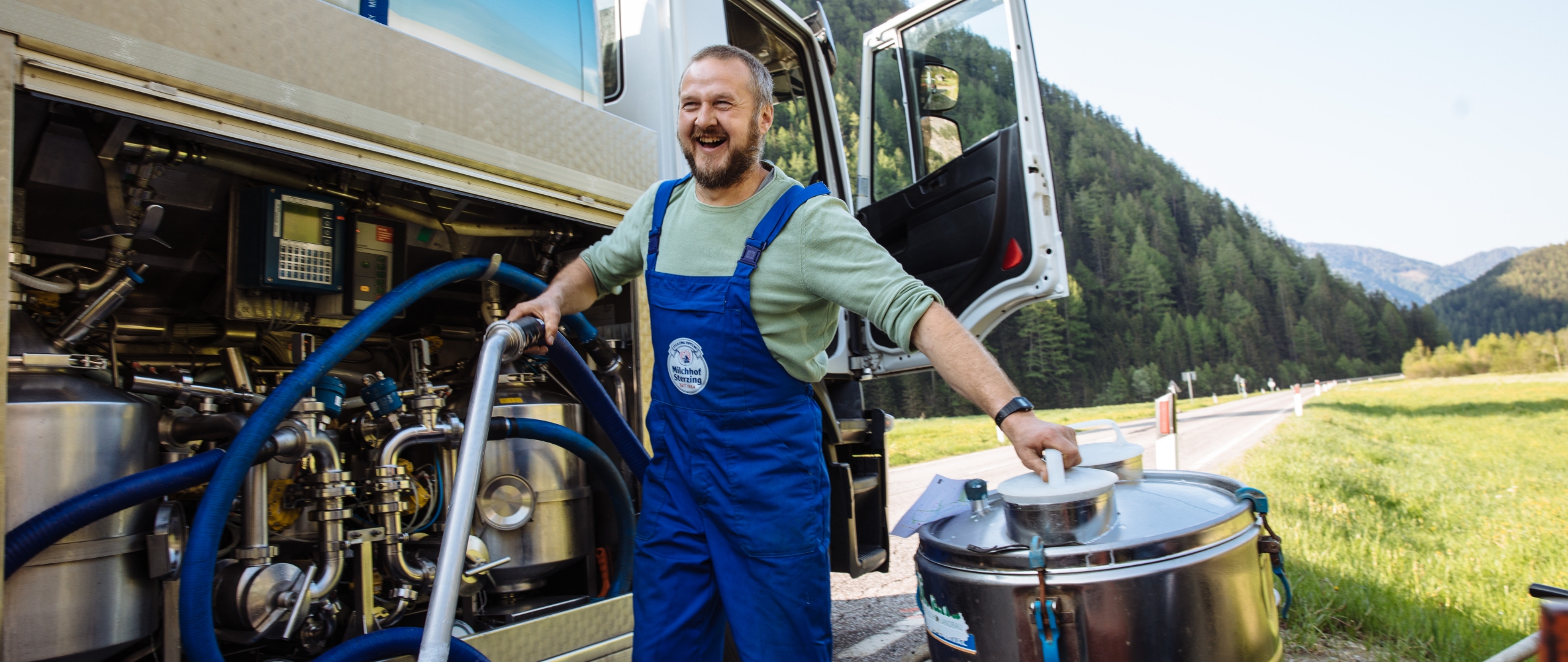 Mitarbeiter von Milchhof Sterzing beim Abpumpen von frischer Milch aus einem Milchsammelwagen vor alpiner Landschaft.