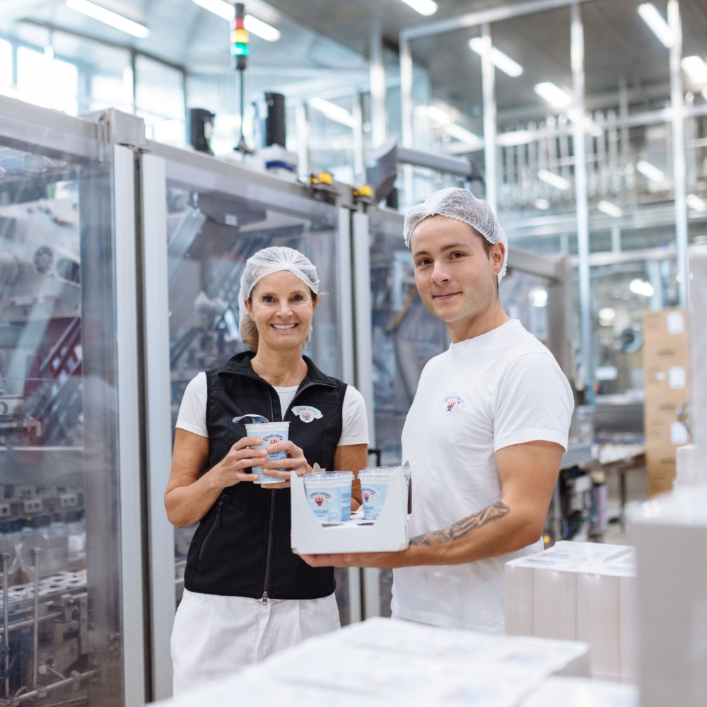 Mitarbeitende in der Molkerei präsentieren abgefüllten Joghurt in der Produktionsanlage