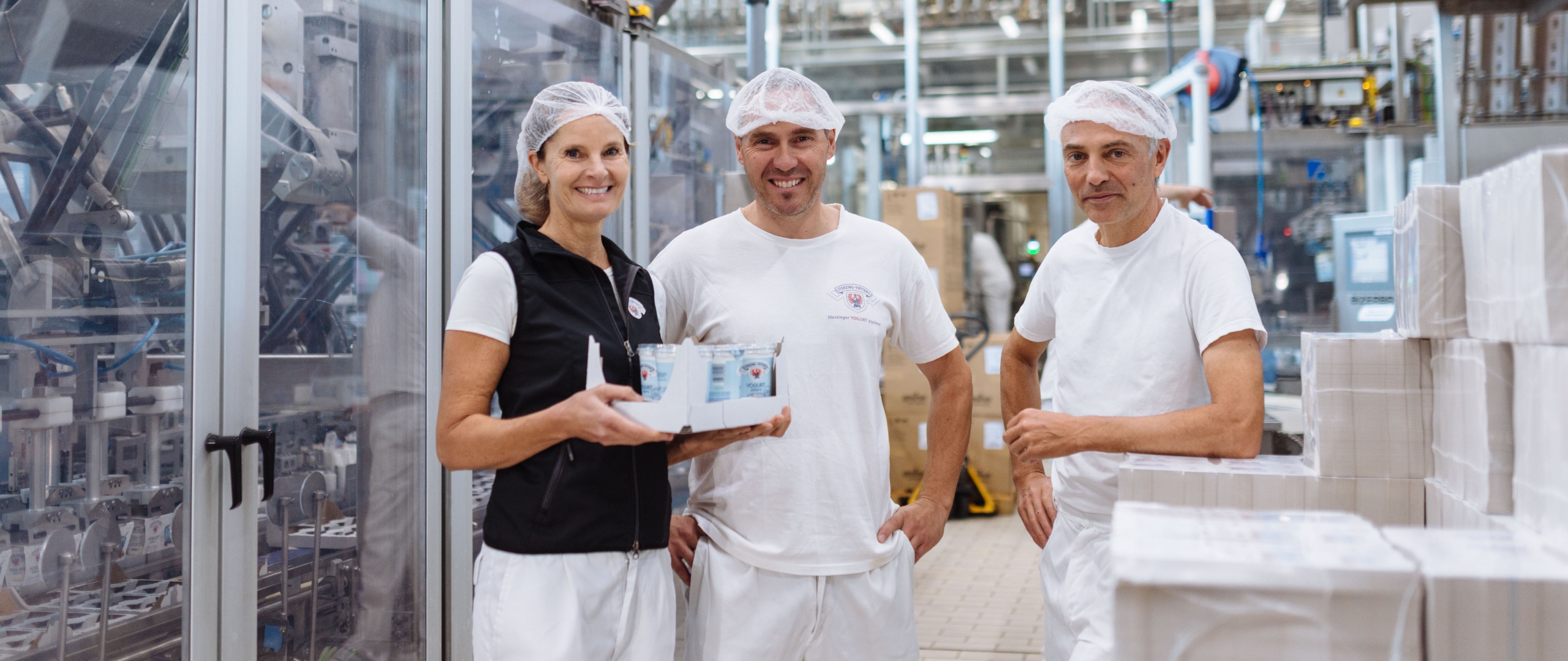 Mitarbeitende in einer Molkerei stehen in der Produktionshalle und halten verpackte Milchprodukte