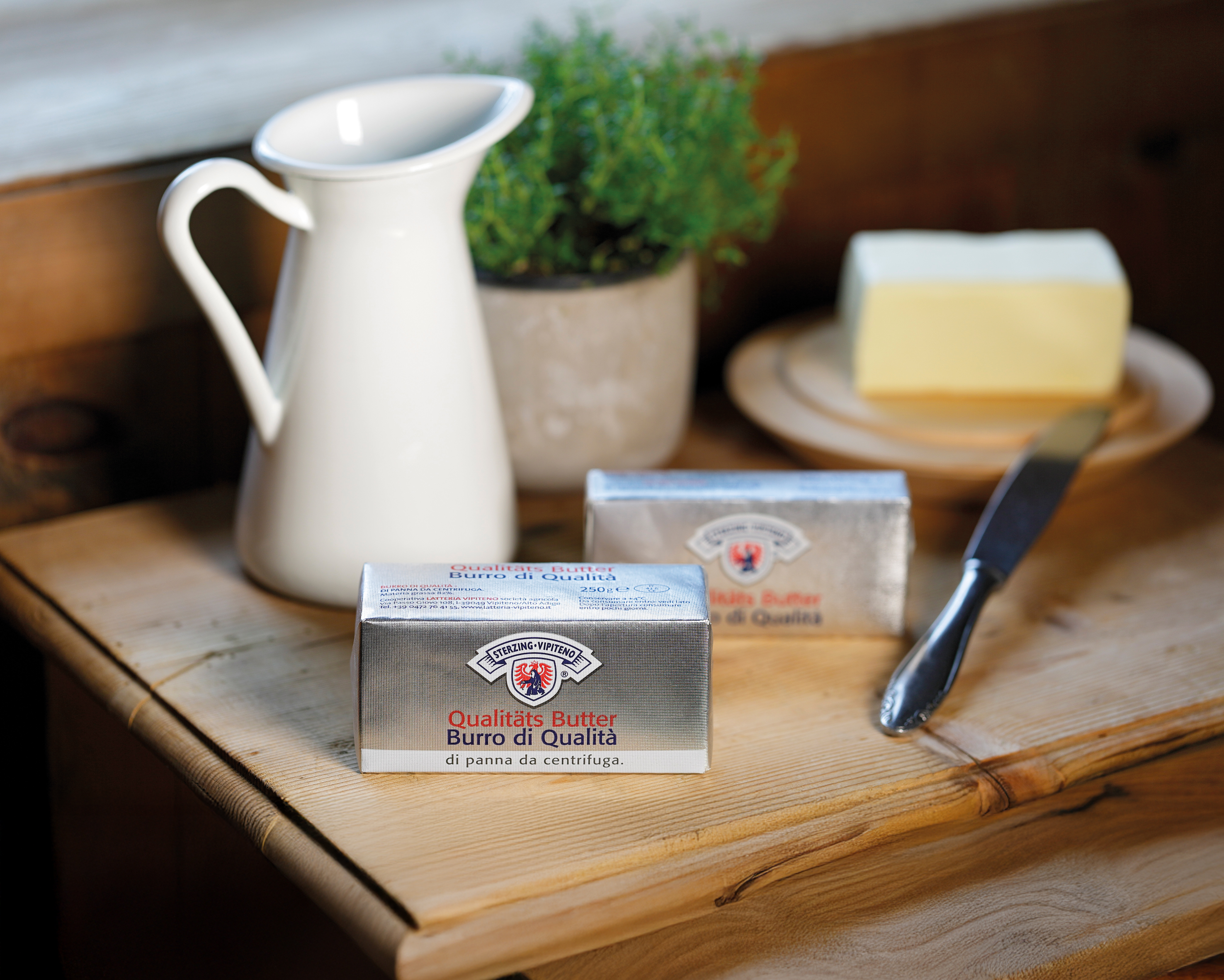 Butter von Milchhof Sterzin in Silberverpackung auf Holztisch mit Milchkrug und Butterstück auf Teller